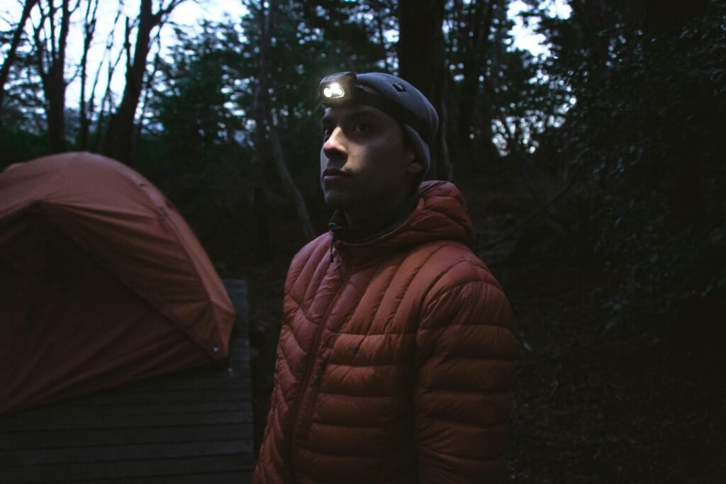 A man with a headlamp in a forest at night, near a tent in Torres del Paine.