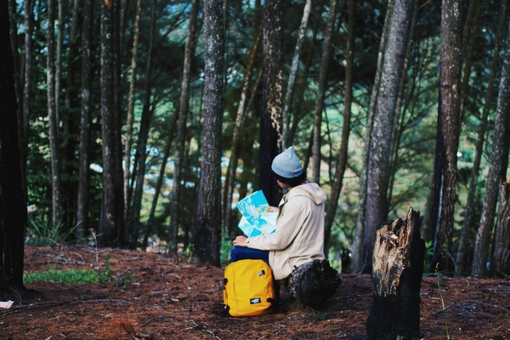 A young adult exploring a forest in Sumatra, Indonesia, with a map, backpack, and beanie hat.