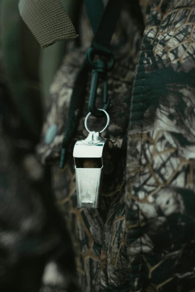 Close-up of a shiny silver whistle hanging against a camouflage-patterned fabric background.